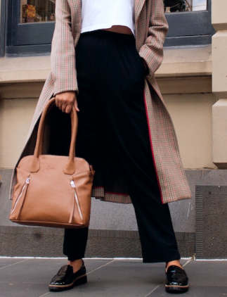 Modelo feminina vestindo uma calça preta e segurando uma bolsa marrom.